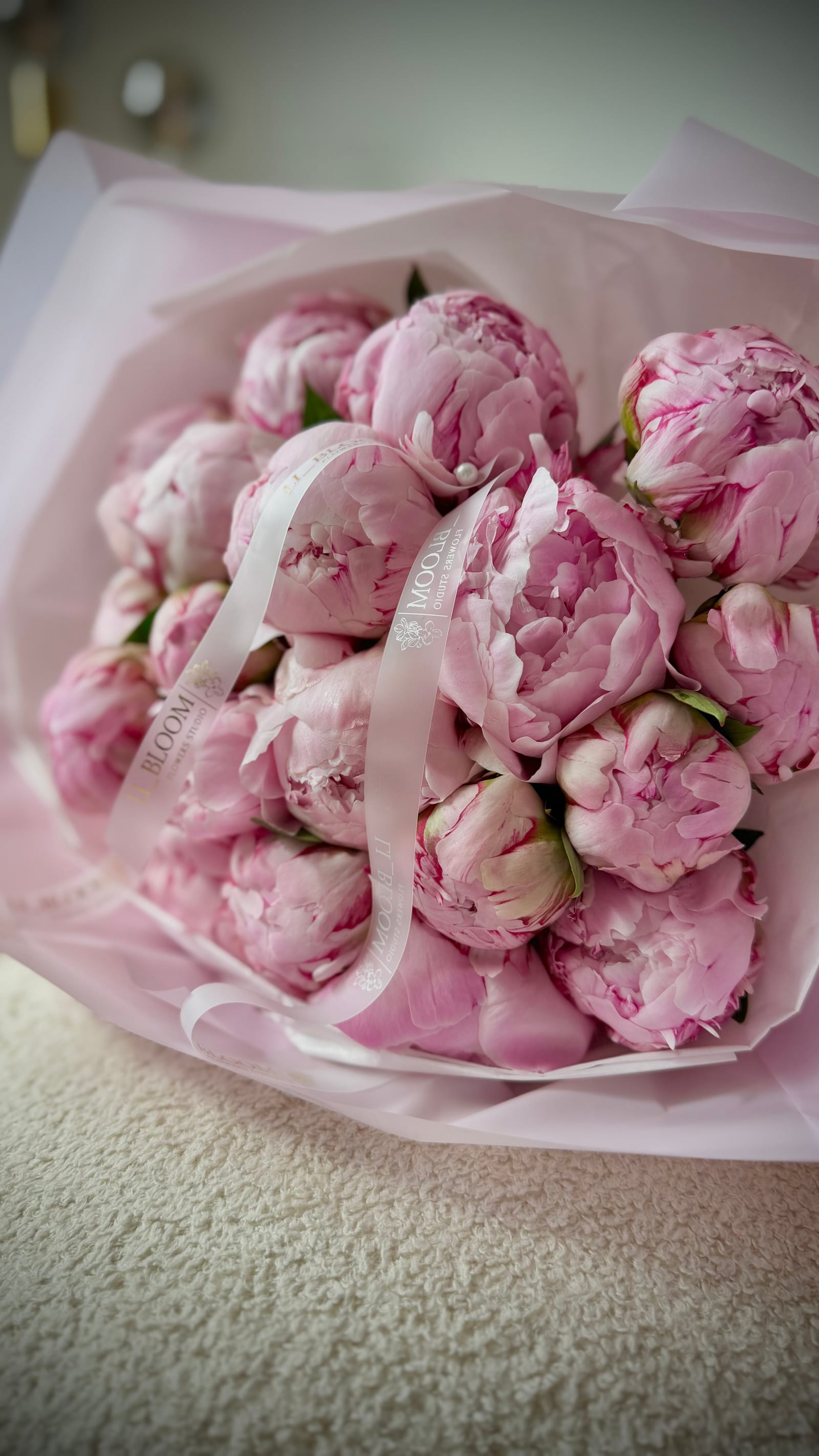 Monostrauß aus rosa Pfingstrosen in hellem Papier, mit einem schmalen Satinband gebunden