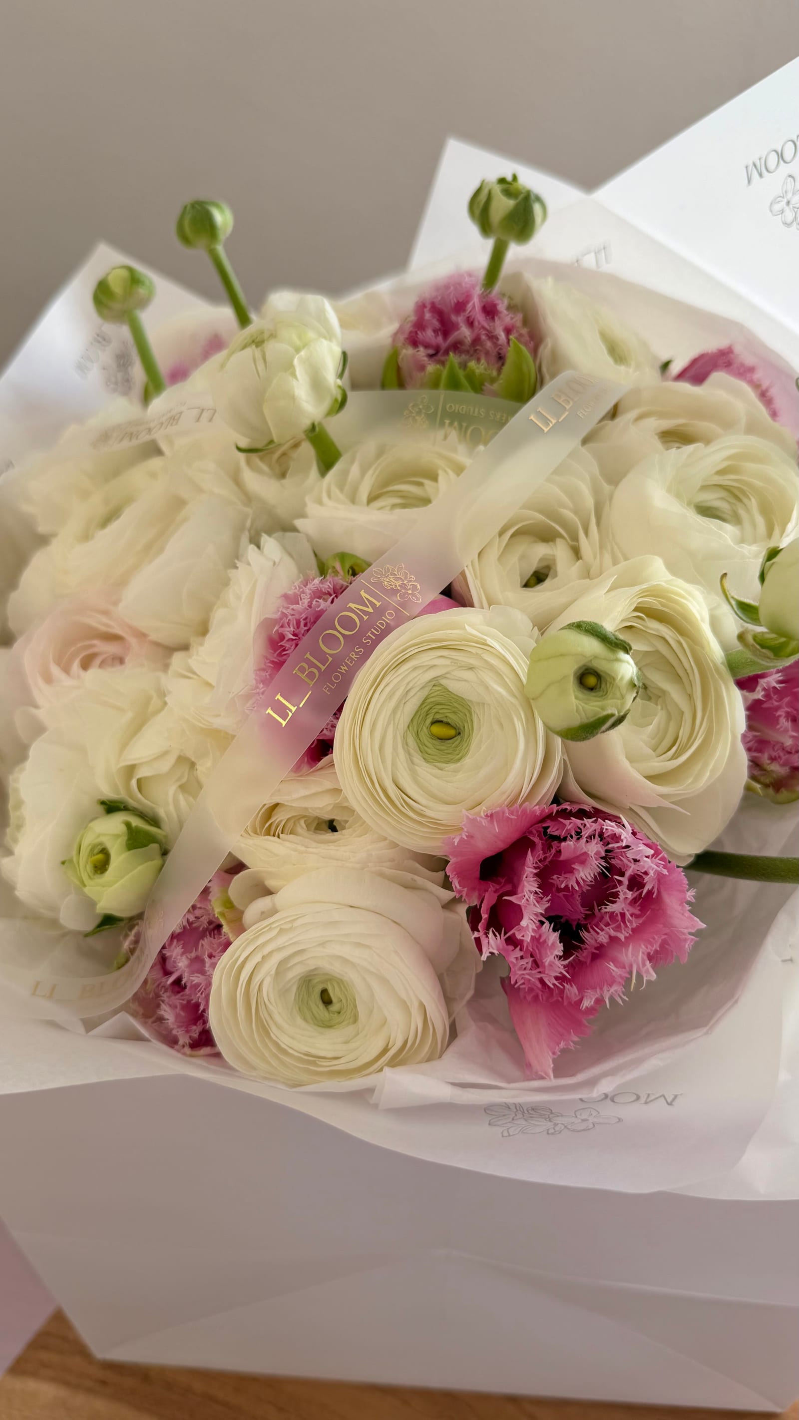 Nahaufnahme eines Straußes aus weißen Ranunkeln und rosa gefransten Tulpen in hellem Seidenpapier