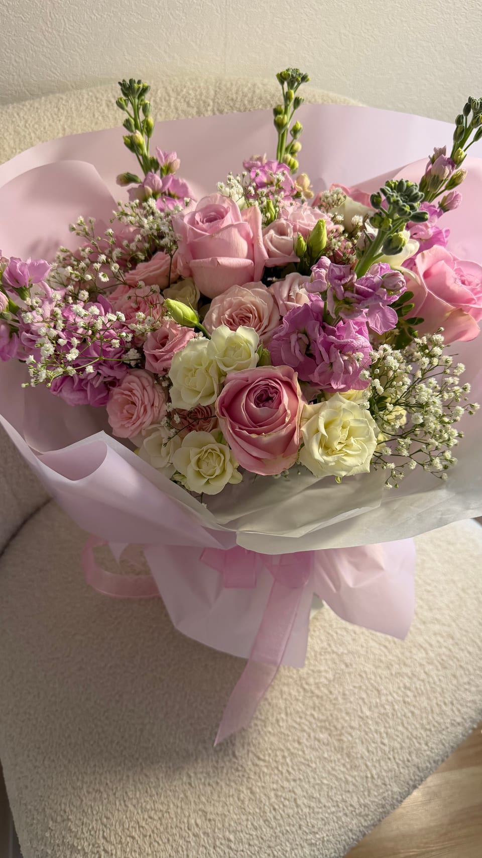 Strauß aus rosa Rosen, Levkojen und Schleierkraut auf einem cremefarbenen Sessel