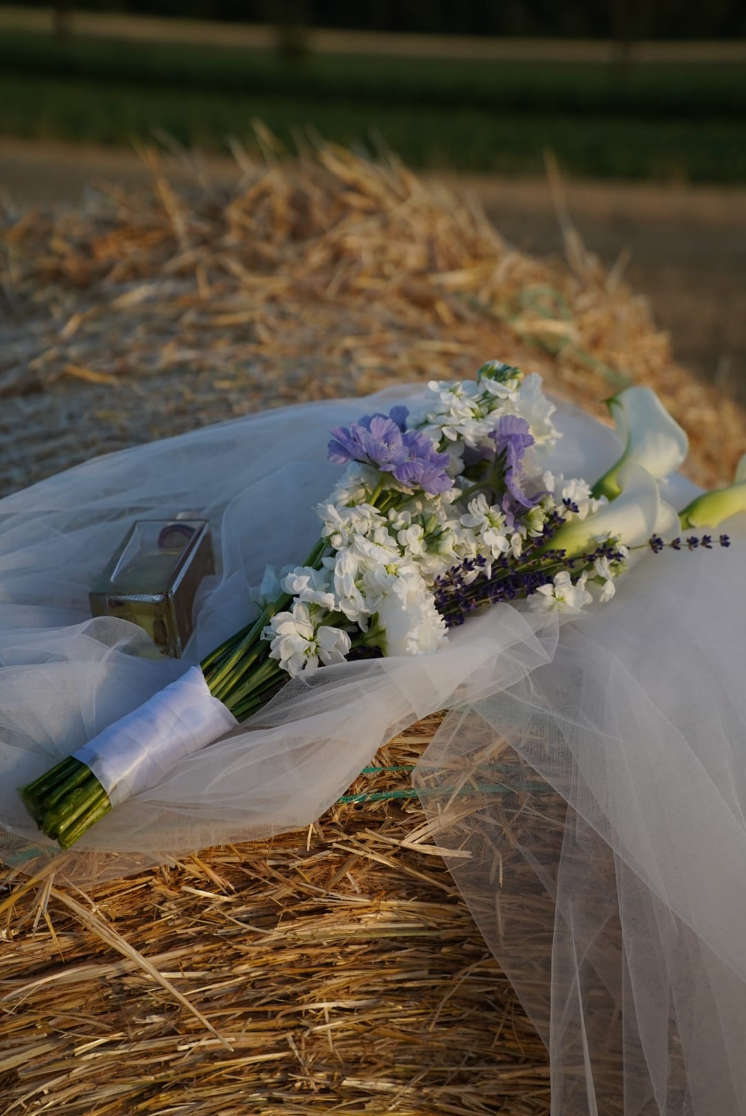 Brautstrauß aus weißen Callas, Levkojen und Lavendel auf Tüll über einem Strohballen