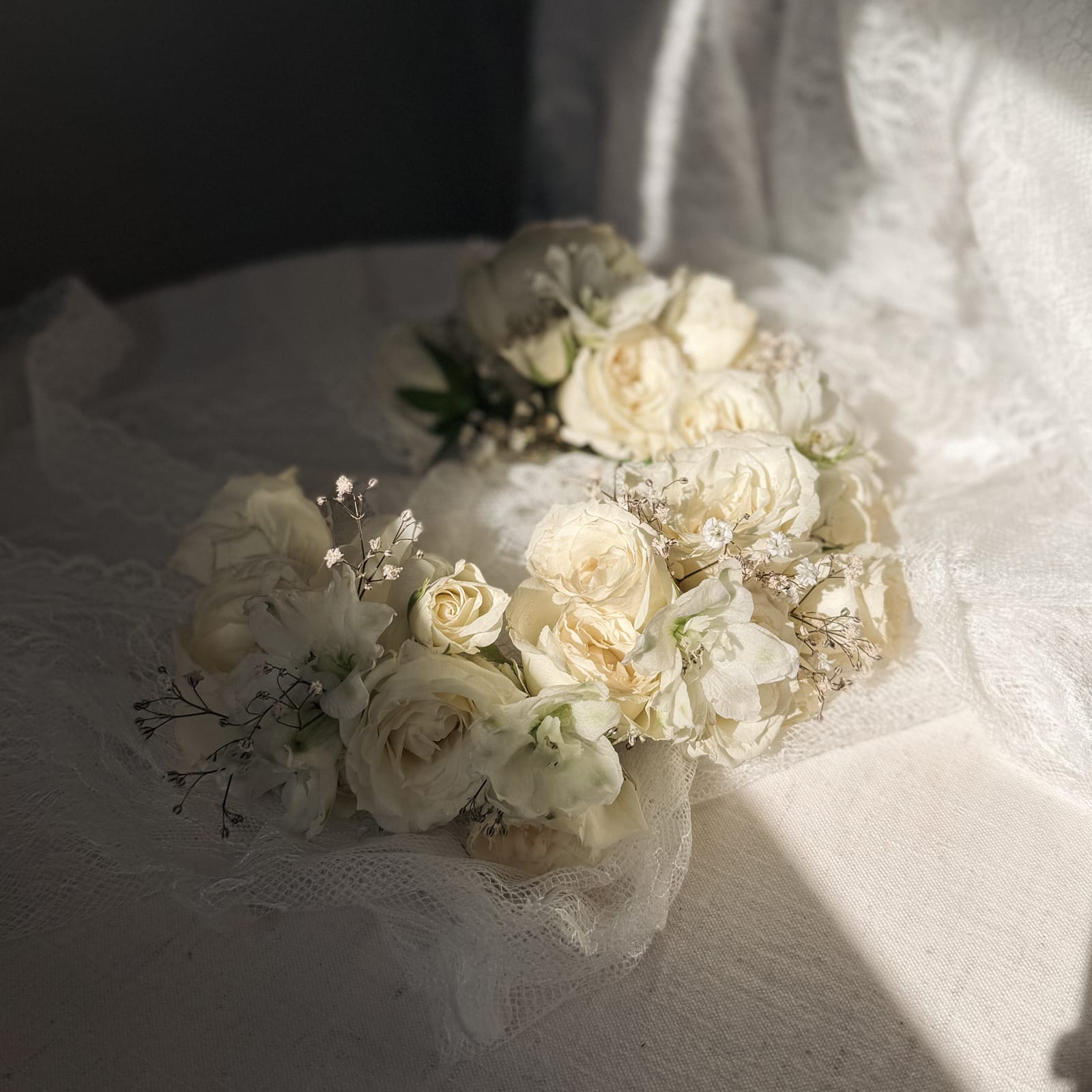 Brautstrauß und floraler Haarschmuck aus cremefarbenen Rosen auf Spitze im Sonnenlicht