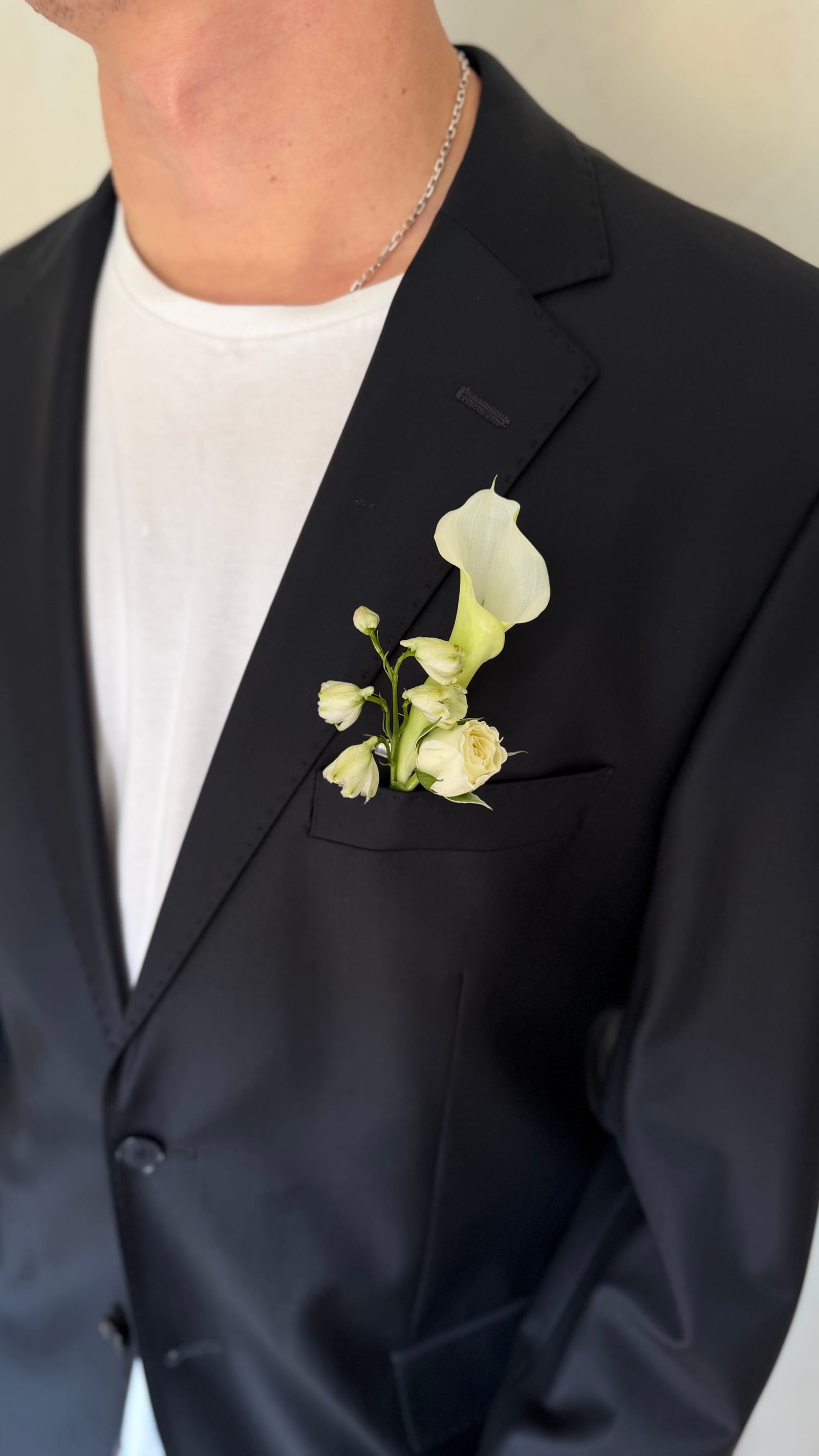 Anstecker mit weißer Calla und Rosen an der Brusttasche eines schwarzen Anzugs