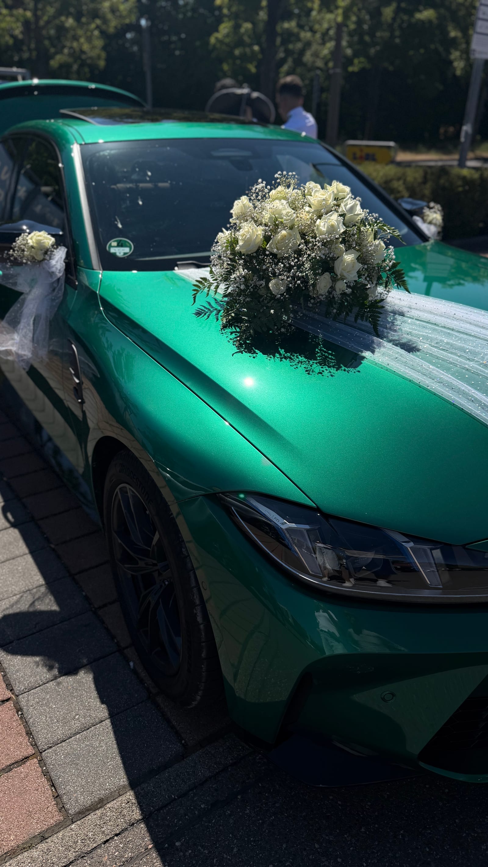 Autoschmuck aus weißen Rosen und Schleierkraut auf der Motorhaube eines grünen Hochzeitsautos