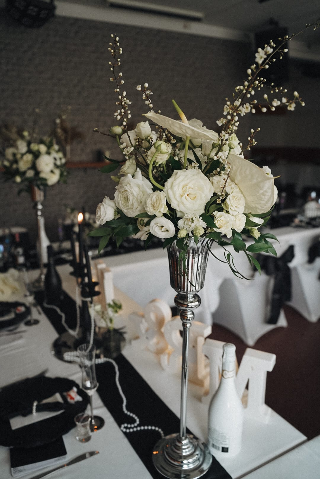 Hohe Tischfloristik aus weißen Rosen und Anthurien auf silbernem Ständer, Tafel in Schwarz und Weiß
